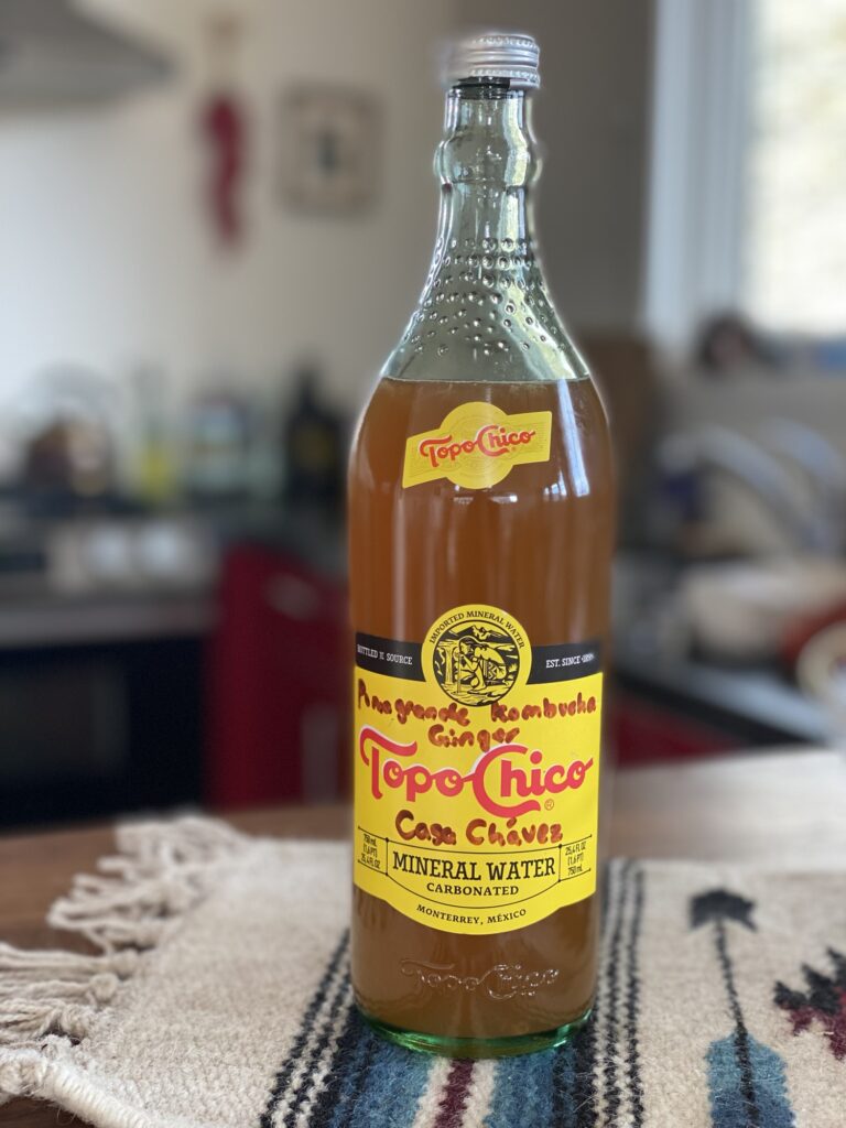 Glass container willed with kombucha resting in a native designed table runner in a kitchen