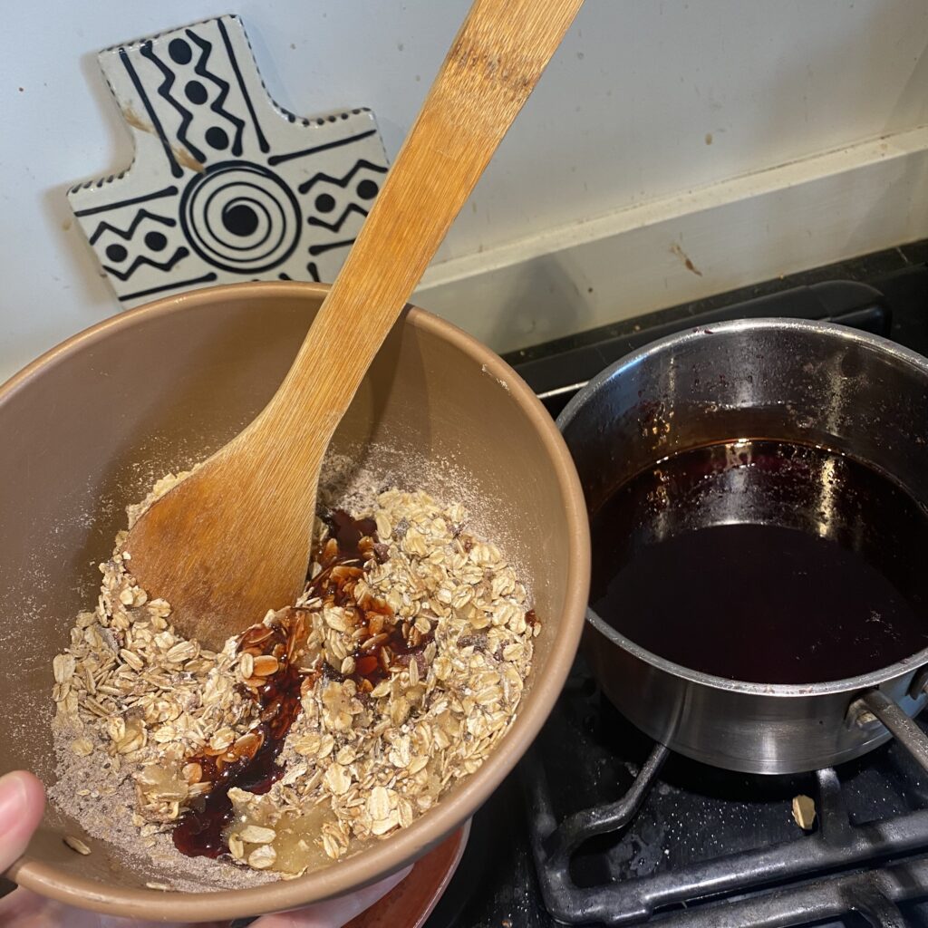 wooden spoon resting in a bowl of oats and pomegranate molasses next to a pot on the stove