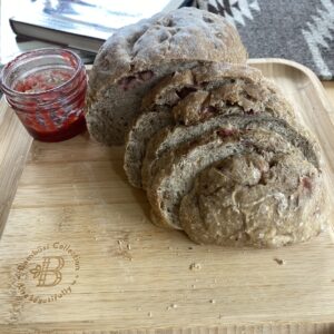 slides bread with bits of strawberry visible on the top arranged next to an almost empty glass jar of strawberry jam on a cutting board