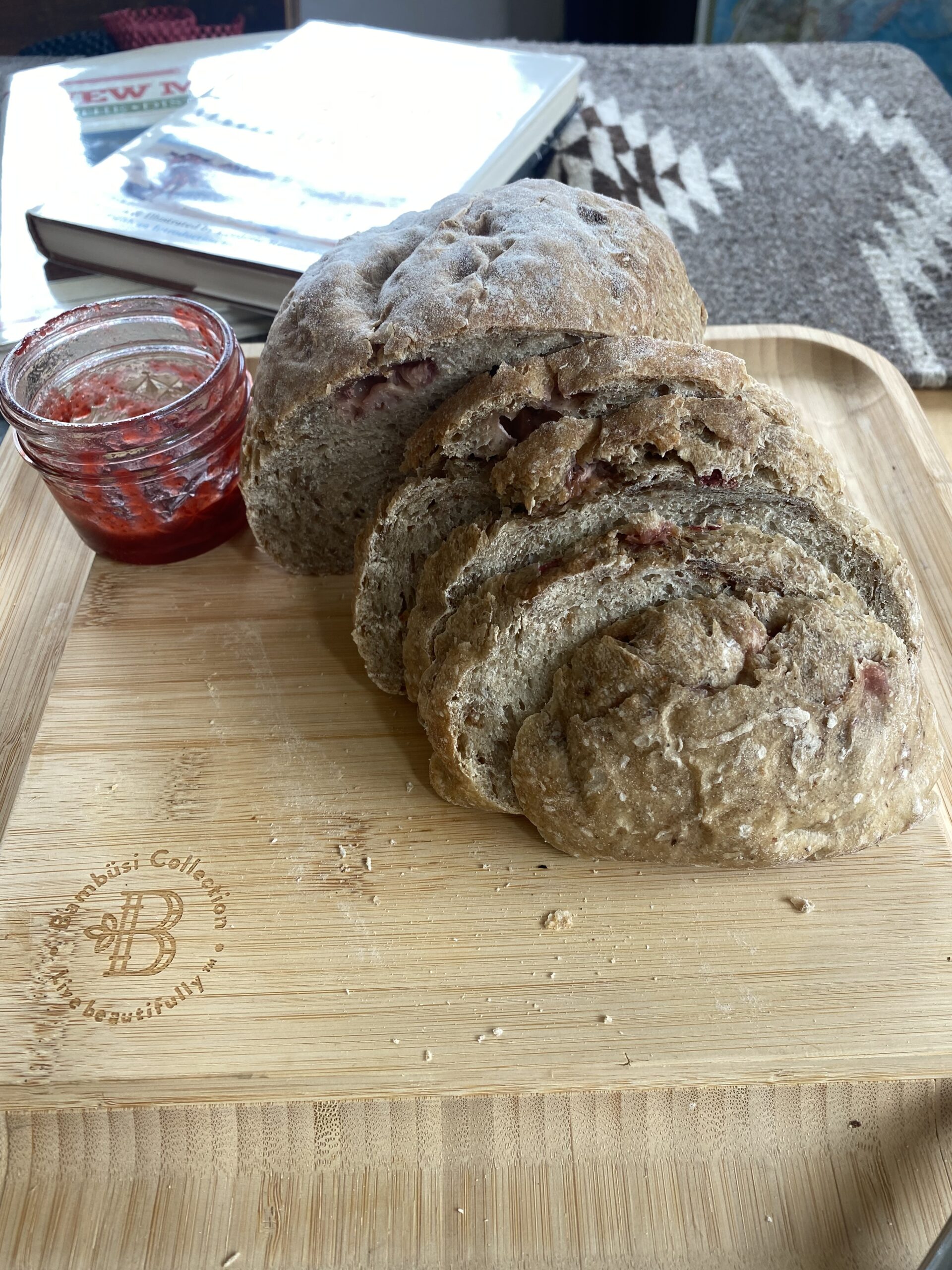 slides bread with bits of strawberry visible on the top arranged next to an almost empty glass jar of strawberry jam on a cutting board