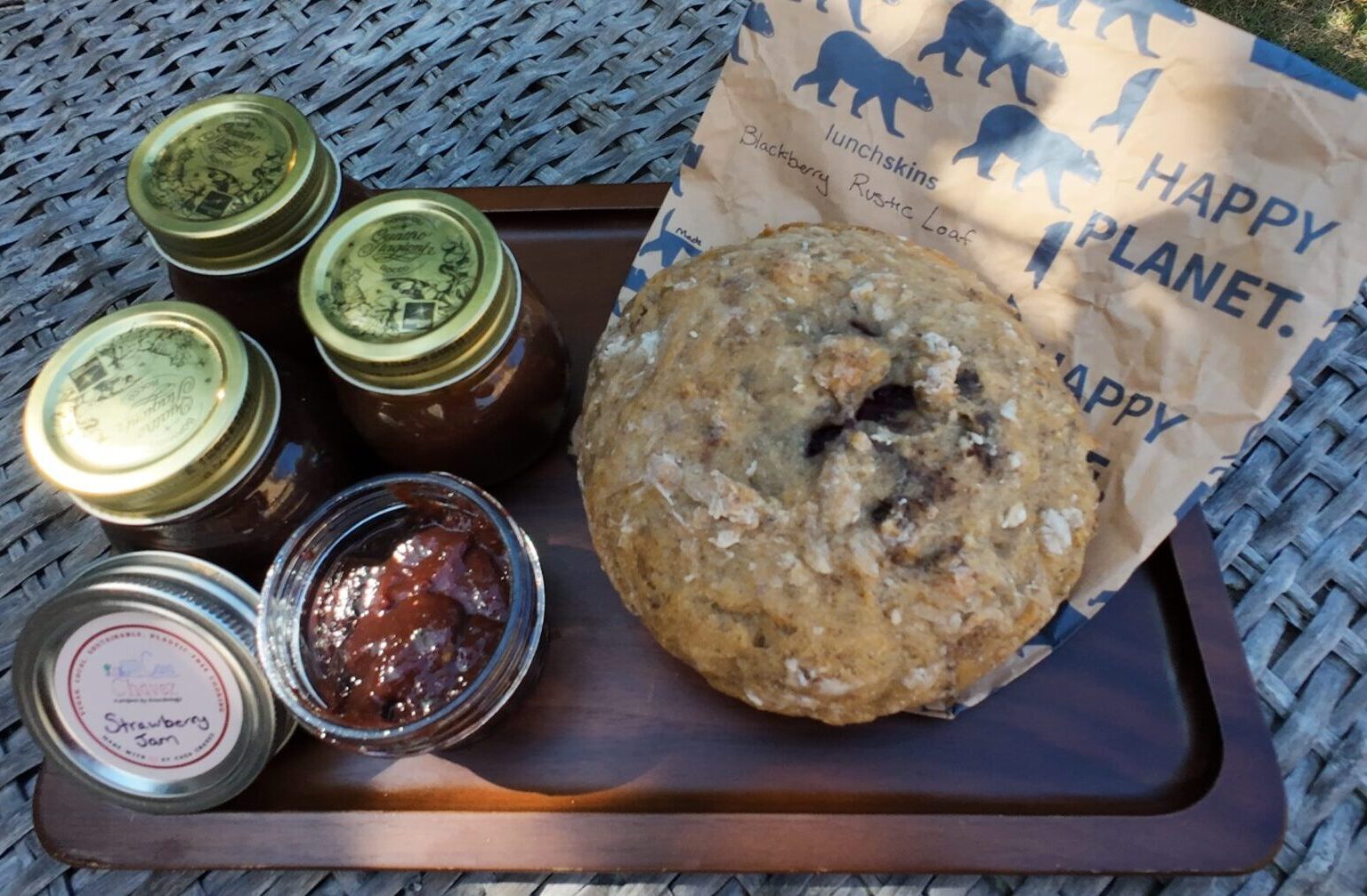 A loaf of blackberry bread next to jars of strawberry and pumpkin spice jam on a picnic table