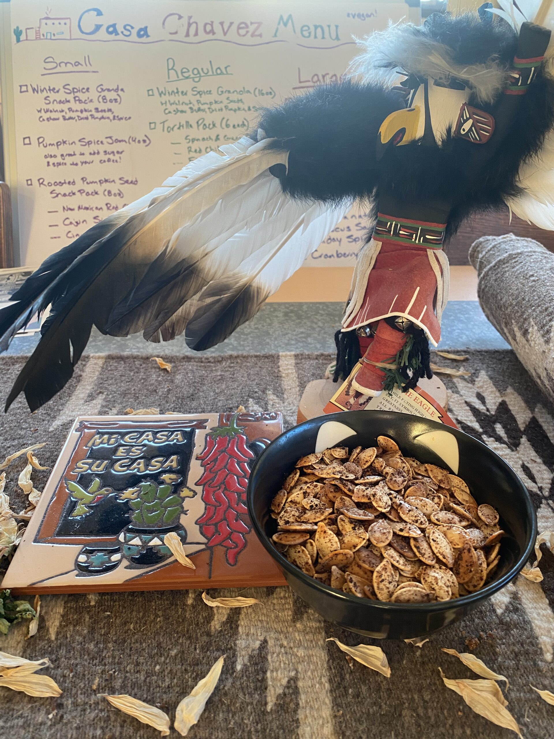 roasted pumpkin seeds with tile that says "mi casa es su casa" and a kachina doll with wings outstretched looking up to the sky
